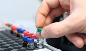 A hand picking up a test tube from a container in a lab. Photo.